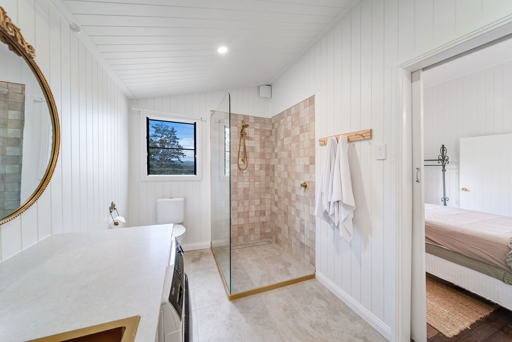 The bathroom after renovation, with white v-groove walls, patterned tile, brass details and a calm vanity.