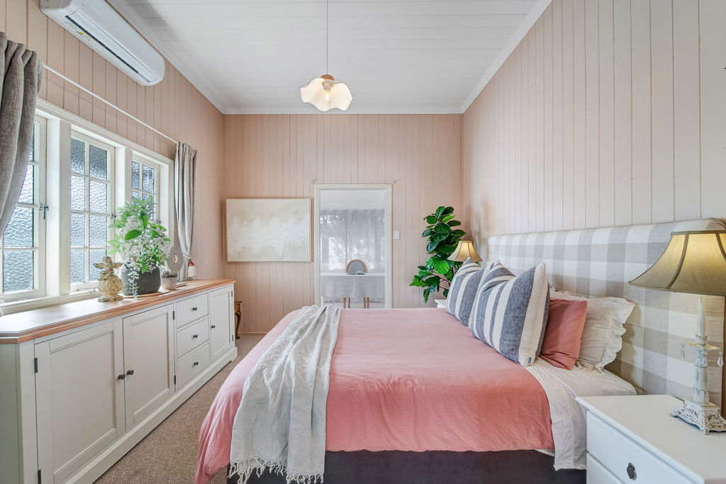 The main bedroom after renovation, with soft pink bedding, pale wall panelling, generous storage and layered textiles.