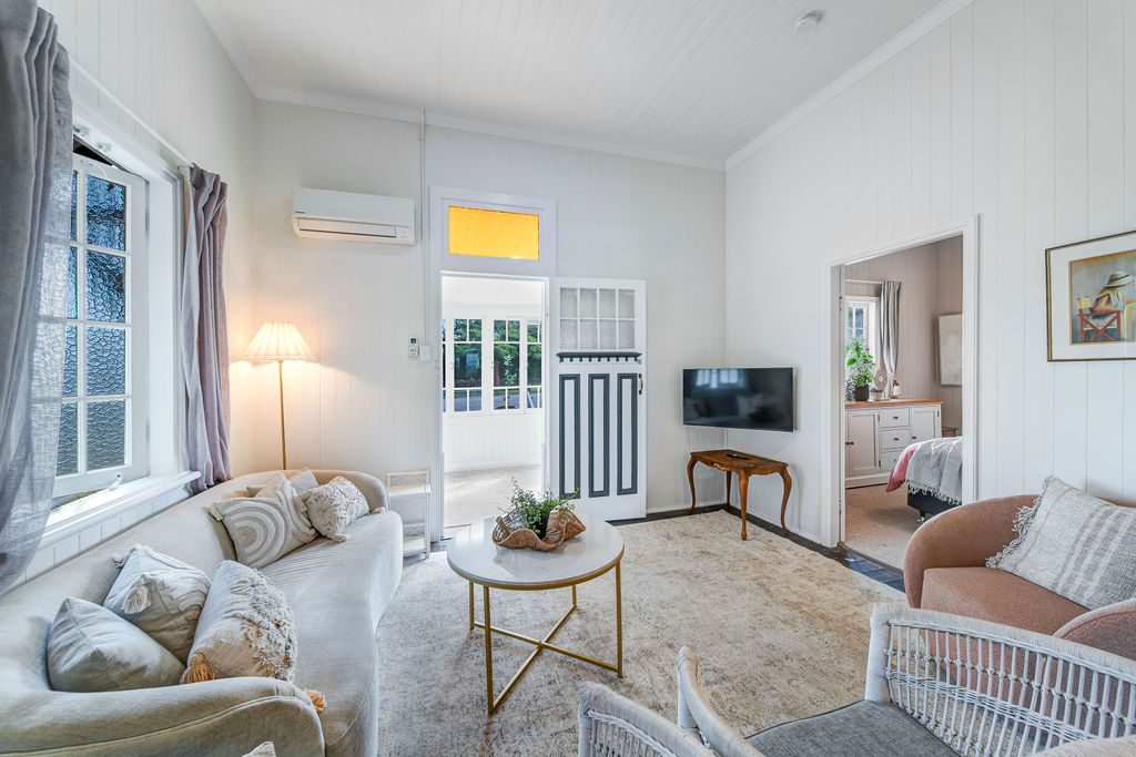 The living room after renovation, with white walls, restored timber floors, soft seating and original timber details.