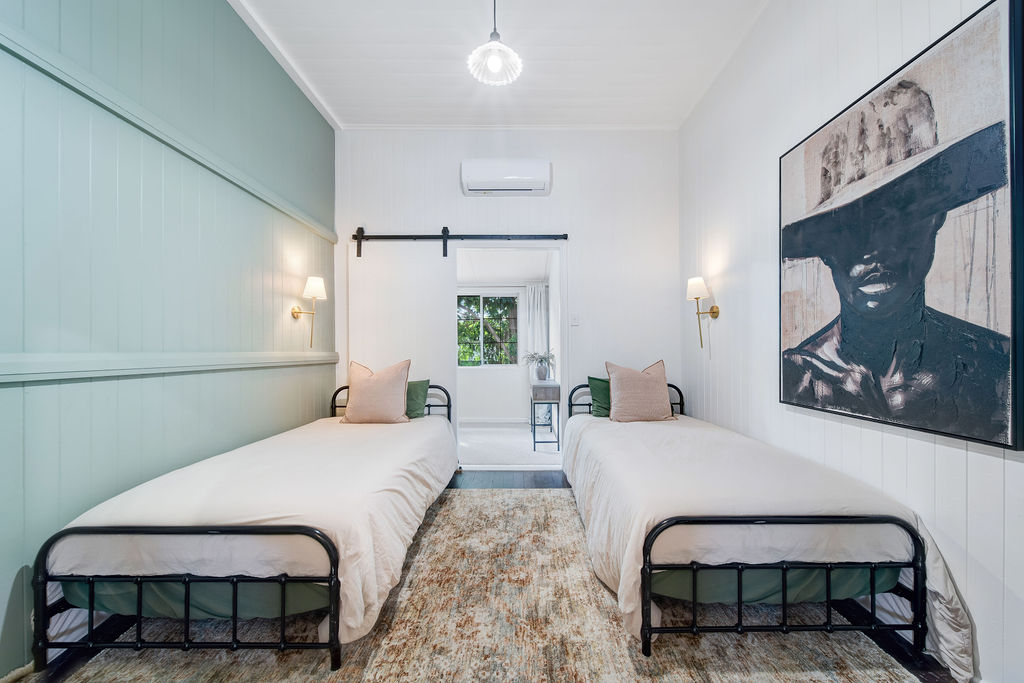 Twin bedroom with green feature wall, white beds and framed artwork.