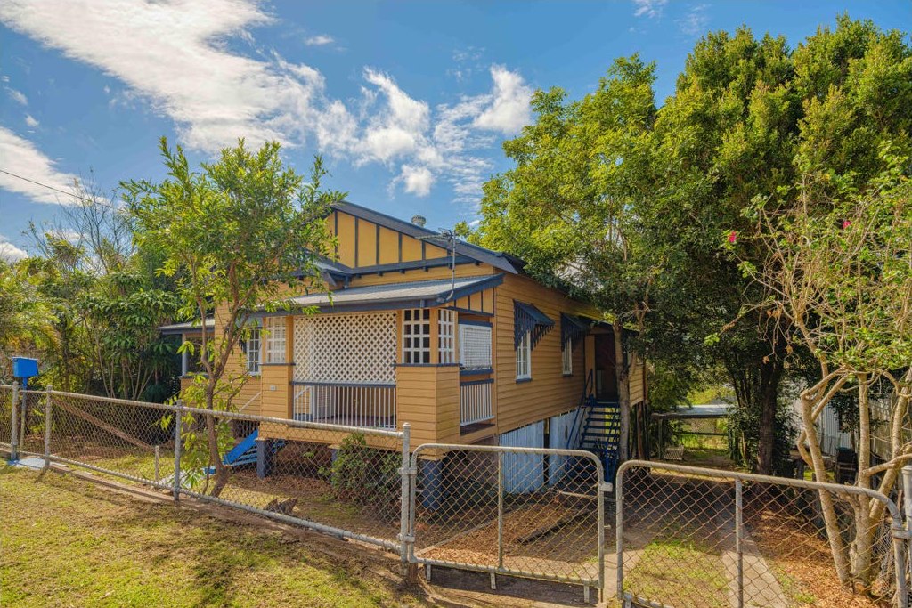 The exterior before renovation, with yellow weatherboards, dark trim and a chain-link fence.