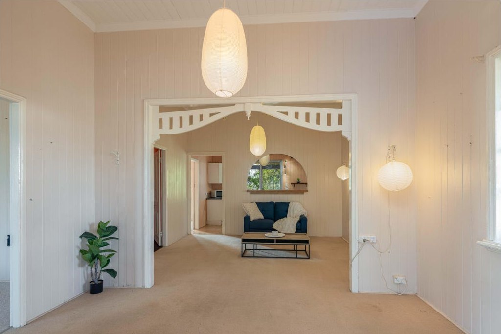 The living room before renovation, with cream carpet, pale wall panelling and a sparse sitting area.