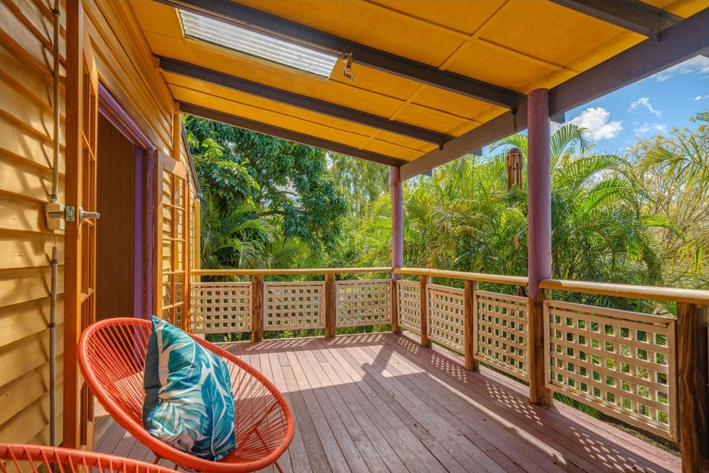 The verandah before renovation, with red posts, lattice balustrade and worn timber boards.