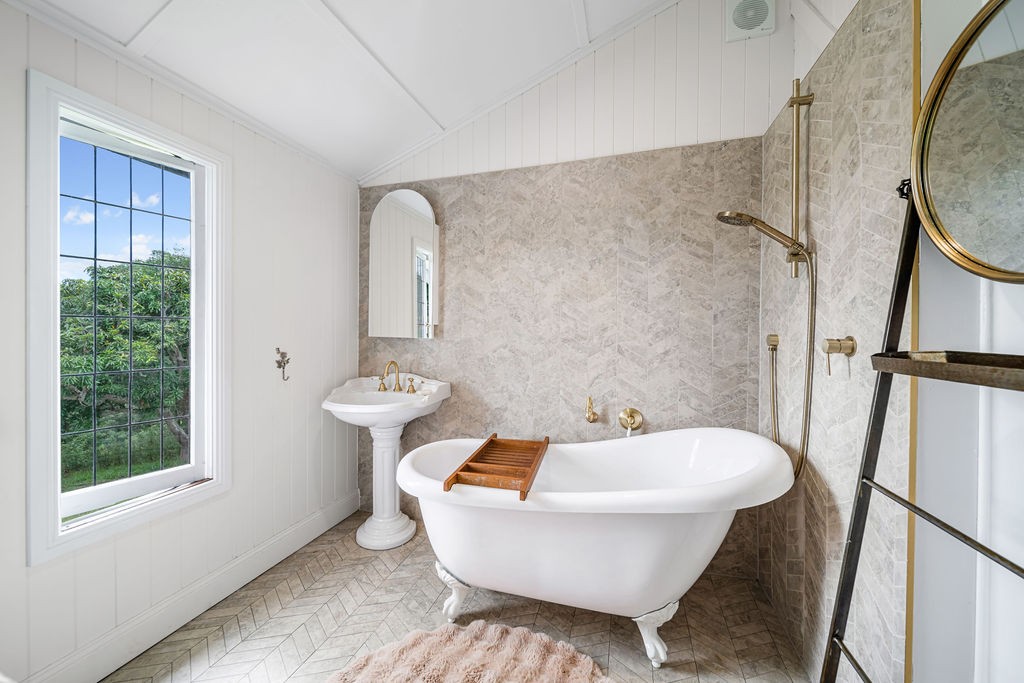 The bathroom after renovation, with a freestanding bath, soft stone-look wall finish and brass fixtures.