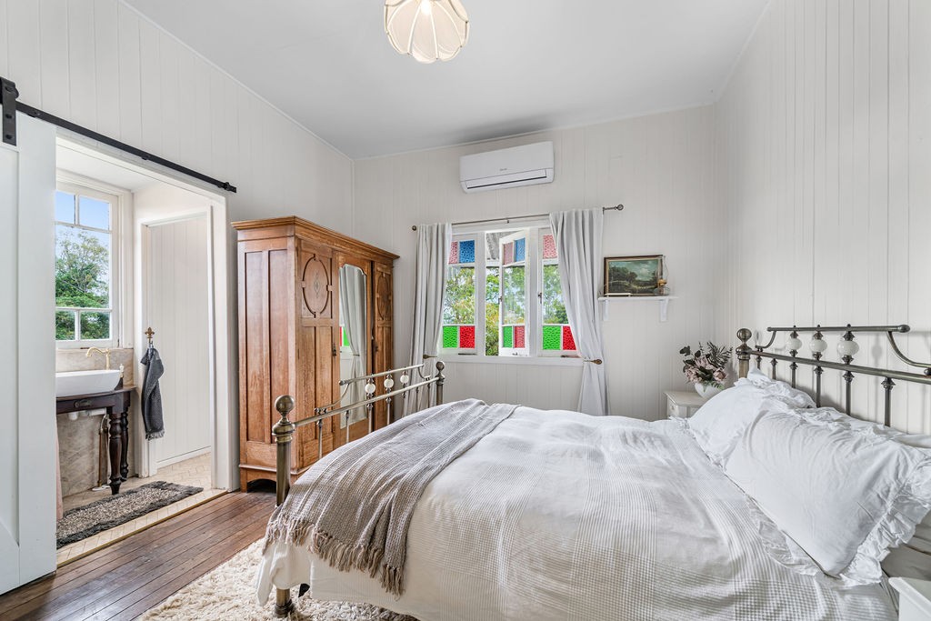 The main bedroom after renovation, with white walls, soft linen and retained coloured glass doors.