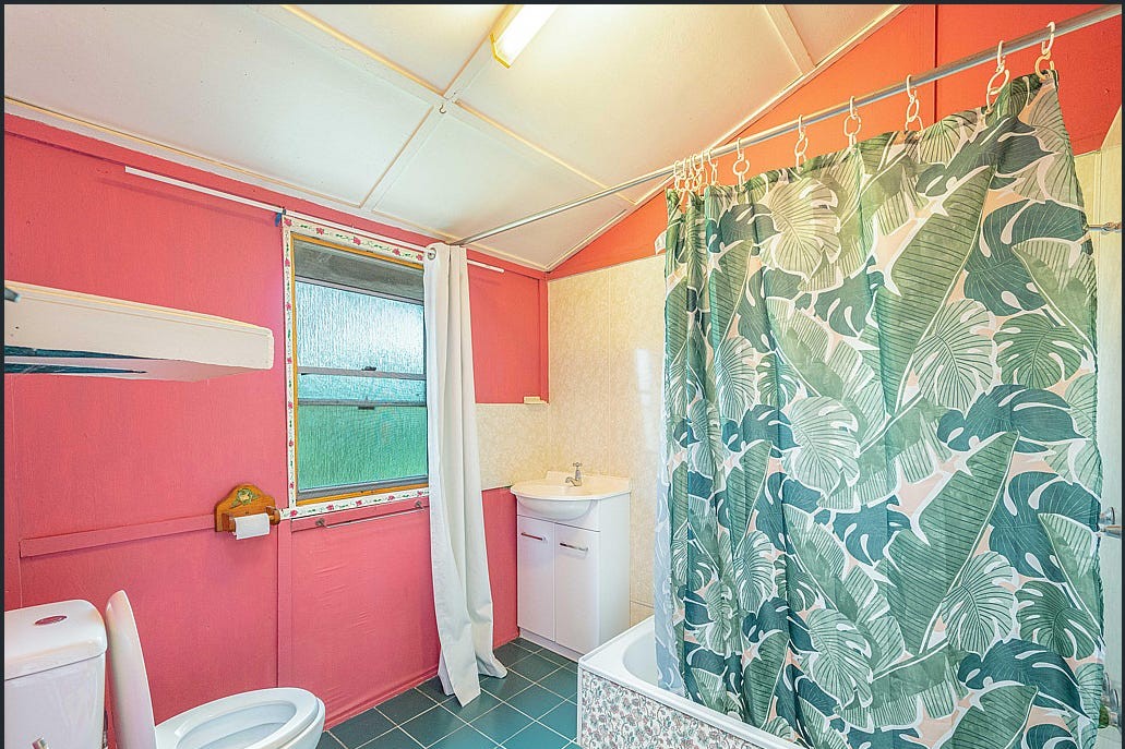 The bathroom before renovation, with red walls, a patterned shower curtain and green floor.