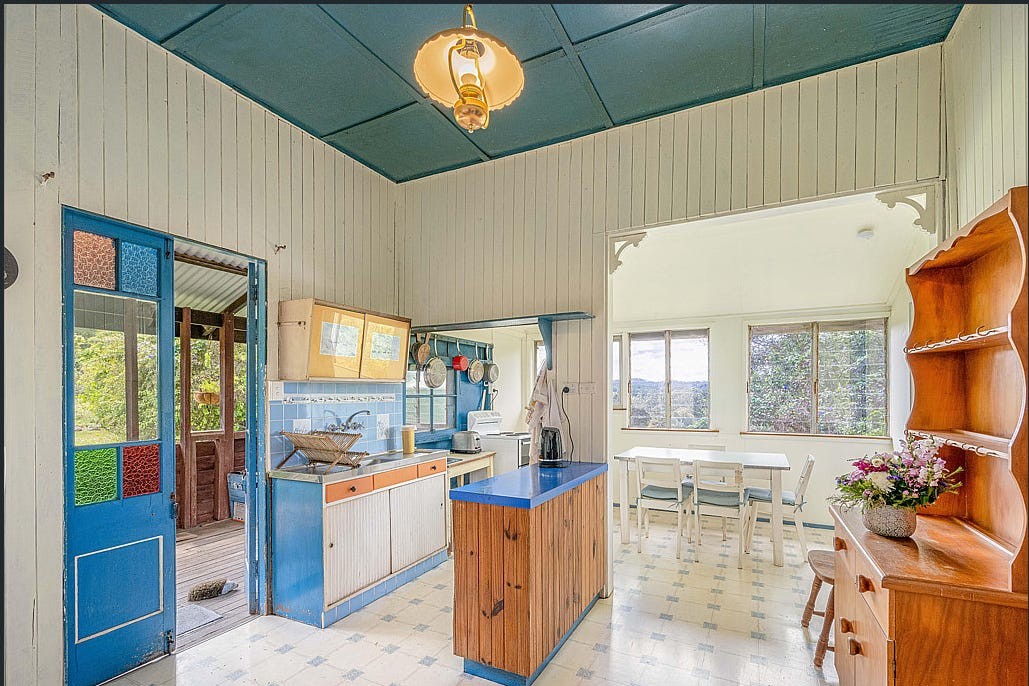 The kitchen before renovation, with blue cabinetry, patterned vinyl flooring and dark ceiling panels.