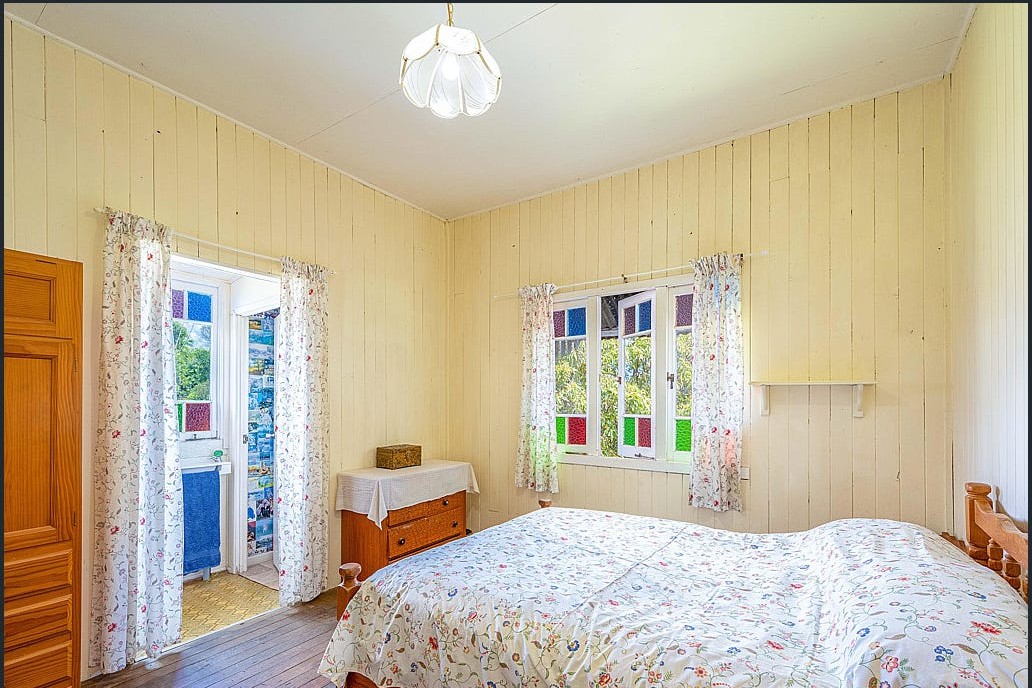 The main bedroom before renovation, with yellow walls, mixed curtains and timber furniture.